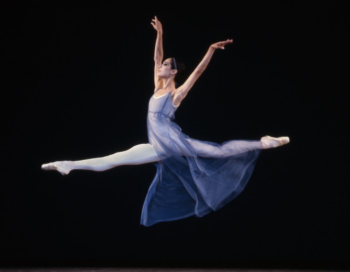 In a steel blue neoclassical dress, Heléne Alexopoulos soars in a grand jeté, her arms over her head.